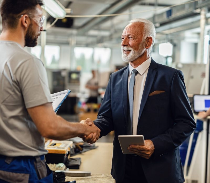 Happy mature company manager handshaking with a worker while visiting factory plant.