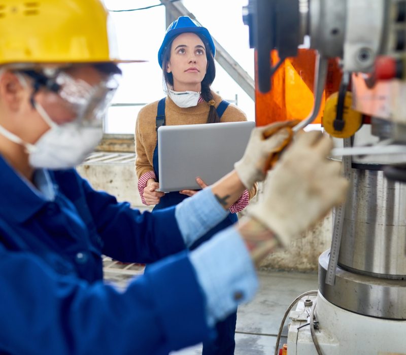 Side view portrait of  young women wearing hardhat and uniform operating  machine units at modern plant, copy space